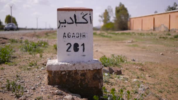 Primer plano del camino de la señal de distancia a Agadir escrito en francés y árabe con el transporte en el fondo. Marruecos — Vídeos de Stock