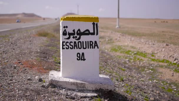 Close-up van afstand teken weg naar essaouira geschreven in Frans en Arabisch talen met carriding op de achtergrond. Marokko — Stockvideo
