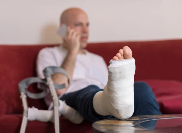 Joven con un tobillo roto y una pierna echada — Foto de Stock