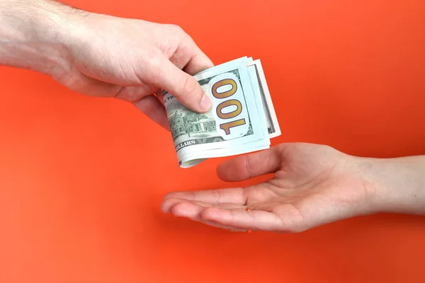 Hand giving folded money usa dollar in other hand on a red background. Bribe concept.
