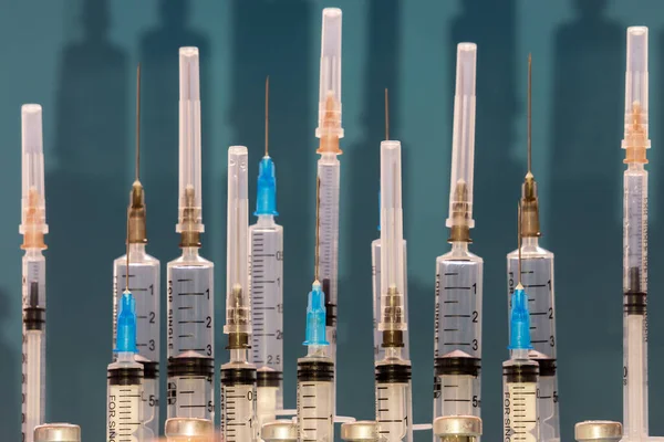 Medical syringes close-up with open and closed needles on a blue background with shadow. The concept of vaccination of the population. Selective focus — Stock Photo, Image