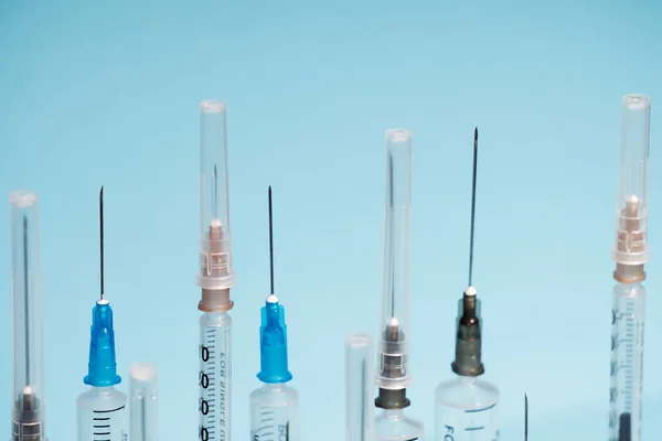 Medical syringes close-up with open and closed needles on a blue monochrome background. The concept of vaccination of the population. Selective focus, a consumable one-time tool — Stock Photo, Image