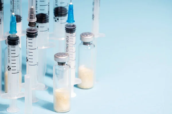 Glass ampoules with medicine in close-up, against the background of medical syringes. The concept of vaccination of the population. Selective focus,copy space, blue solid background — Stock Photo, Image