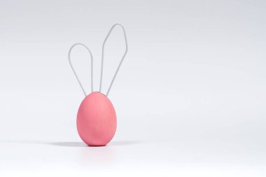 Kulakları havada, beyaz telden yapılmış pembe Paskalya yumurtası. Paskalya Tavşanı Konsepti. Yumuşak gölgeli, yakın plan beyaz izole arkaplan
