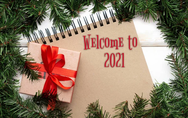 Welkom bij 2021.Bruin spiraalvormig notitieboekje, geschenkdoos met een rode strik op de achtergrond van een frame van kersttakken. Close-up, kopie van de ruimte — Stockfoto