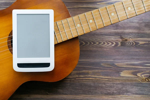 Part of a guitar, tablet on a brown wooden background. Close-up, copy space, mock up. The concept of online guitar courses.