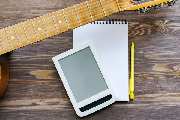 A piece of guitar, fingerboard, tablet, notepad and yellow pencil on a brown wooden background. Close-up, copy space, mock up. The concept of online guitar courses.