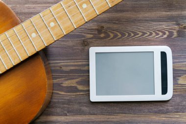 Kahverengi bir gitarın parçası ve yanında yatay olarak yerleştirilmiş beyaz bir tablet. Kahverengi ahşap zemin, kopyalama alanı, düzen. Online gitar kurslarının reklamları..