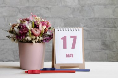 17 Mayıs. Ayın 17 'si, takvim randevusu. Pembe bir vazoda bir buket çiçek, iki kurşun kalem ve tahta bir yüzey üzerinde günü olan bir takvim...