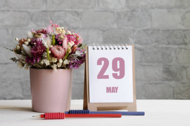 29 Mayıs. Ayın 29 'u, takvim tarihi. Pembe bir vazoda bir buket çiçek, iki kalem ve tahta bir yüzey üzerinde günü olan bir takvim...