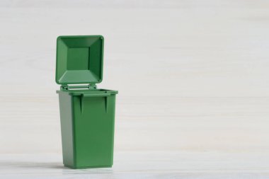 Boş yeşil renkli konteynır, çöpü ayırmak için, açık kapaklı, beyaz ahşap arka planda yakın plan. Daha fazla işlemek için çöp, atık ayıklama kavramı.