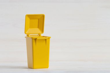 Çöp ayıklamak için boş sarı konteynır, kapağı açık, yakın plan beyaz ahşap arka plan. Daha fazla işlemek için çöp, atık ayıklama kavramı.