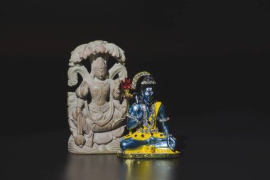 Two Buddhist figurines, Shiva and Buddha, on a black isolated background. Close-up, banner, copy space.