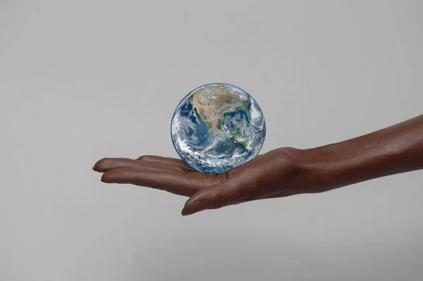 Dark-skinned hand holds the planet in the palm of its hand. Gray isolated background, space for copying. Elements of this image furnished by NASA. The concept of the world is in your hands.