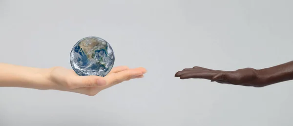 The white hand holds the earth planet in the palm of its hand and holds it out to the dark-skinned hand. The concept of equality, friendship, peace of peoples and races.
