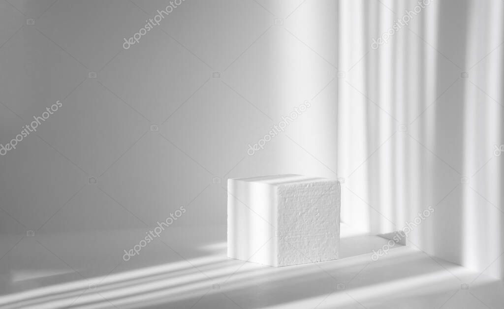 3d podium, for presentations of packaging and cosmetics. White foam cube against background of clean walls, shadow from the harsh sunlight, as stripes.