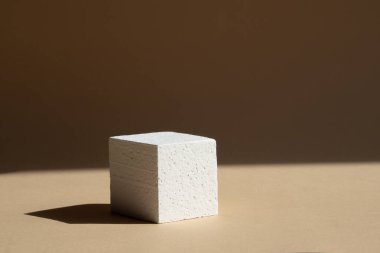 Paketleme ve kozmetik sunumları için 3D podyum. Kahverengi arka planda, doğal ışıktan sert bir gölgesi olan beyaz köpük küpü. Güzellik endüstrisi konsepti.
