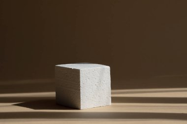 Paketleme ve kozmetik sunumları için 3D podyum. Pencereden süzülen sert gölgeli beyaz köpük küpü. Kahverengi arkaplan ve güneş ışığından gelen koyu çizgiler. Güzellik endüstrisi kavramı.