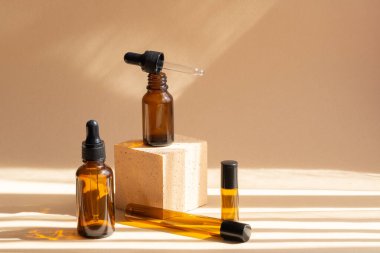 Kozmetik ürünleri, doğal ilaçlar ve 3 boyutlu podyumda gerekli yağlar için çeşitli cam şişeler. Güneş ışığından gelen gölgelerle bej bir arka plan. Vücut bakımı ve kaplıca kavramı.