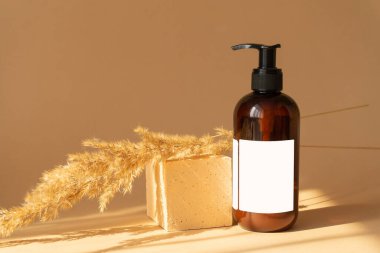 Kare bej standı, iki tutam kuru otla, plastik şişe kozmetik için, gün ışığında. Pencerenin sert gölgeleriyle sıcak bir arka plan. Güzellik endüstrisi kavramı.