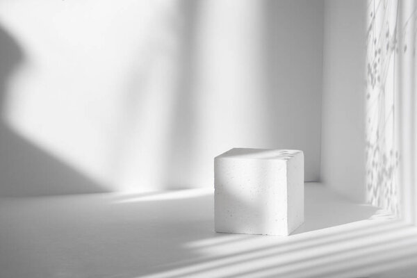 Белый куб на фоне чистых стен при солнечном свете. Твердые тени от солнечных лучей, в виде полос различной ширины. Концепция 3D подиума для презентаций упаковок и косметики.