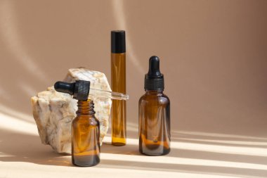 Boş kahverengi cam şişeler, açık ve kapalı damlalar, kozmetik için, yağlar, kremler, mermer taşın yanında duruyor. Nesnelerin yumuşak gölgeleri bej arkaplana düşer