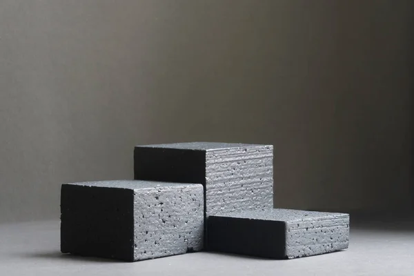 Three black square stands, of different heights, on black background. Platforms for presentation of products and cosmetics. Concept of the beauty industry. 3d podium made of geometric shapes.