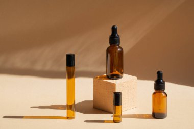 Çeşitli şekillerde kahverengi cam şişeler, karenin üstünde yükseklikler, ürünlerin sunumu için. Güneş ışığıyla bej renkli pastel arka plan. Nesnelerin gölgesi masanın yüzeyine düşer.