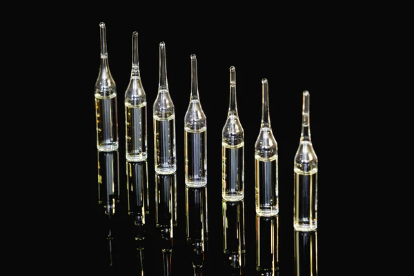 Medical ampoules for injection, isolated on black background with reflection. Ampoules with vaccine, medicine, collagen, vitamins, clear liquid.