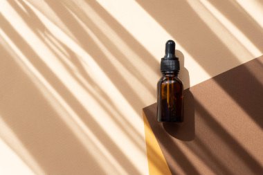 Soyut çok renkli arka planda güneş ışığı ışınlarıyla cam damlatıcının maketi. Kahverengi ve turuncu kağıt çarşaflardan yapılmış doğaçlama 3D podyum. Vücut bakımı kavramı.