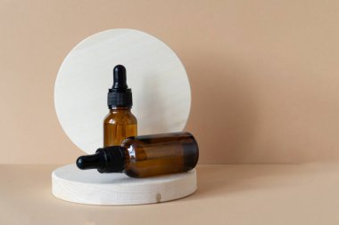 Ürünü sergilemek için yuvarlak ahşap standın üzerine damlatan kapaklı iki kahverengi şişenin maketi. Kozmetik ürünlerin sunumu için 3D podyum kavramı. Yakın plan, bej arkaplan