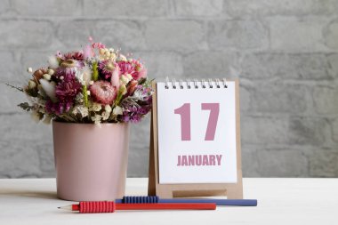 17 Ocak. Ayın 17 'si, takvim randevusu. Pembe bir vazoda bir buket çiçek, iki kurşun kalem ve tahta bir yüzey üzerinde günü olan bir takvim...