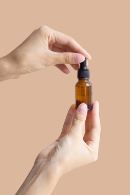 Kadın eli, bej arka planda cam damlatan şişenin maketini tutuyor. Yakın plan, kopyalanacak yer, dikey görüntü. Vücut bakımı, kaplıca tedavisi kavramı.
