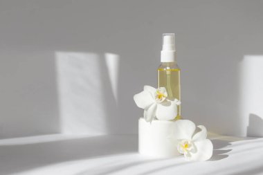 Krema kavanozunun maketi, orkide çiçekleriyle çevrili cam şişe. Beyaz arka plan ve sabah güneşleri. Cilt bakımı, kaplıca tedavisi, doğal kozmetik ürünleri.