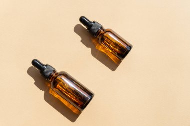 Kahverengi arka planda, güneş ışığı ışınlarında iki sahte damlalık şişesi yüzeyde sert bir gölge oluşturur. Güzellik endüstrisi kavramı, düz yatış.