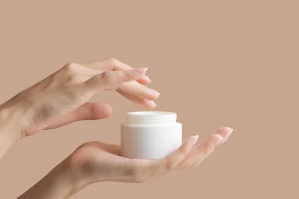 Woman\'s hand dips her finger into mock-up of white package with cream. Concept of body care, beauty industry