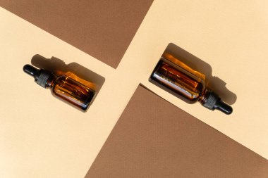 İki şişe damlatıcısı iki yaprak kahverengi kağıdın arasına rastgele yerleştirilmiş. Nesnelerin sert gölgesi bej arkaplanın yüzeyine düşer.