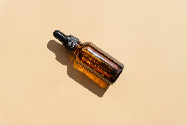 Flat lay of dropper bottle mockup with hard shadows. Close-up of oil bottle in sunlight on beige background. Concept of beauty industry, body care.