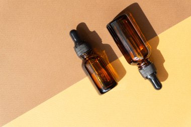 Güneş ışığının sert gölgesi olan iki şişe maketi. Düz, turuncu-kahverengi arka plan. Vücut bakımı kavramı, doğal kozmetik ürünleri, spa tedavileri.