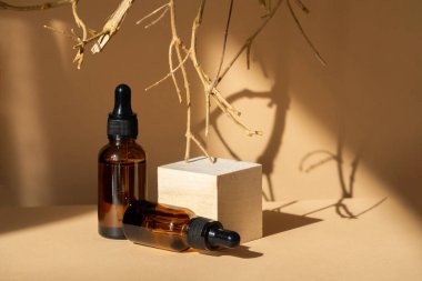 Üç boyutlu ahşap podyum, iki cam damlatıcı şişesi ve sallanan kuru ağaç dalı, kahverengi arka planda, güneş ışığı altında. Güzellik endüstrisi kavramı