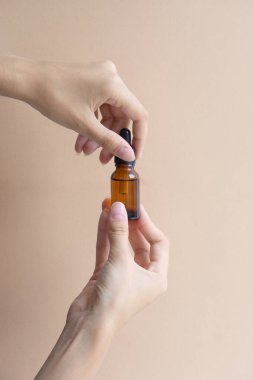 Kadınların elleri cam damlatan şişenin maketini tutuyor ve bej arka planda vidaları söküyor. Dikey görüntü, yakın plan. Vücut bakımı, spa tedavileri, doğal kozmetik ürünleri