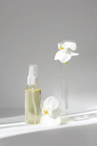 Dikey görüntü, cam şişenin temel yağ ve sabah ışıklarıyla beyaz arkaplanda orkide çiçekleri bulunan test tüpüyle maketi. Cilt bakımı kavramı, doğal kozmetik. — Stok fotoğraf