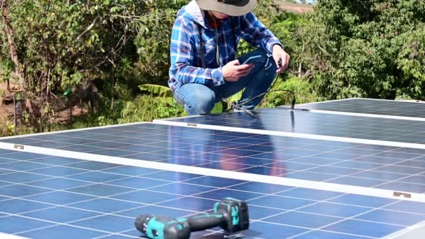 Hombre instalación de paneles solares en una casa en la azotea para energía limpia fotovoltaica mediante la búsqueda de conocimientos de Internet con el teléfono móvil antes de instalar — Vídeos de Stock