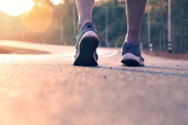 Yolda koşan sporcu, gün batımında koşmadan önce ısınmak için yavaş yürüyüş için bacağına yaklaş..