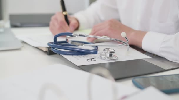 Stetoscopio su un tavolo in una sala d'esame medico. Medico scrivere una prescrizione o record paziente esaminare i risultati per il paziente. Concetto di medicina sanitaria — Video Stock