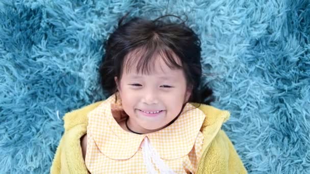 Asijské holčička usmívající se pohled na kameru, když ji leží na koberci doma — Stock video