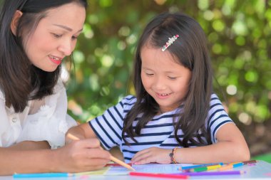 Anne kızı Asyalı çocuklara ev bahçesinde ya da parkta ödev yapmayı öğretiyor. Ev okulu konsepti.