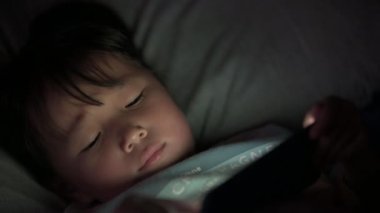 Küçük kız çocuklar gece akıllı bir telefonda oyun oynuyorlar ekrandan yansıyan ışıklar, tablet bağımlısı Asyalı küçük kız, çocuk teknolojisi konsepti.