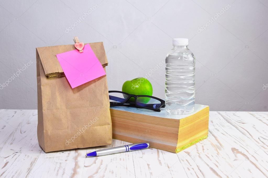 paper  lunch bag  with apple,water and books  on desk with post-it note