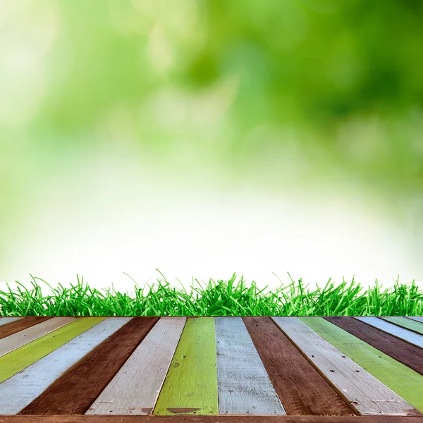 Frisches frühlingsgrünes Gras mit blauem Bokeh und Sonnenlicht und Holzboden. Natürlicher Hintergrund — Stockfoto